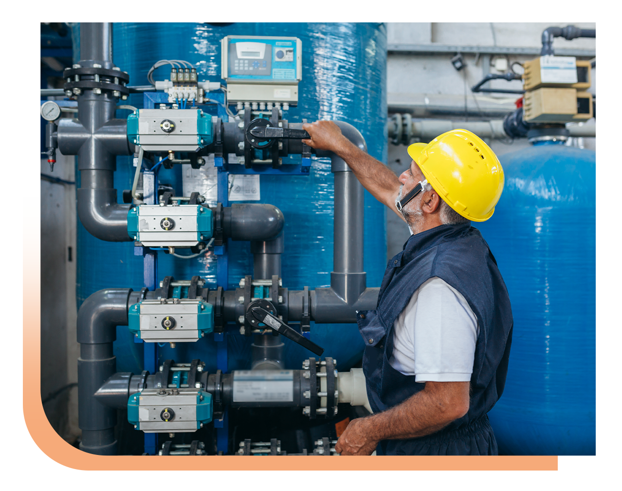 Maintenance worker in a yellow hard hat adjusts blue industrial valves and piping in a plant setting