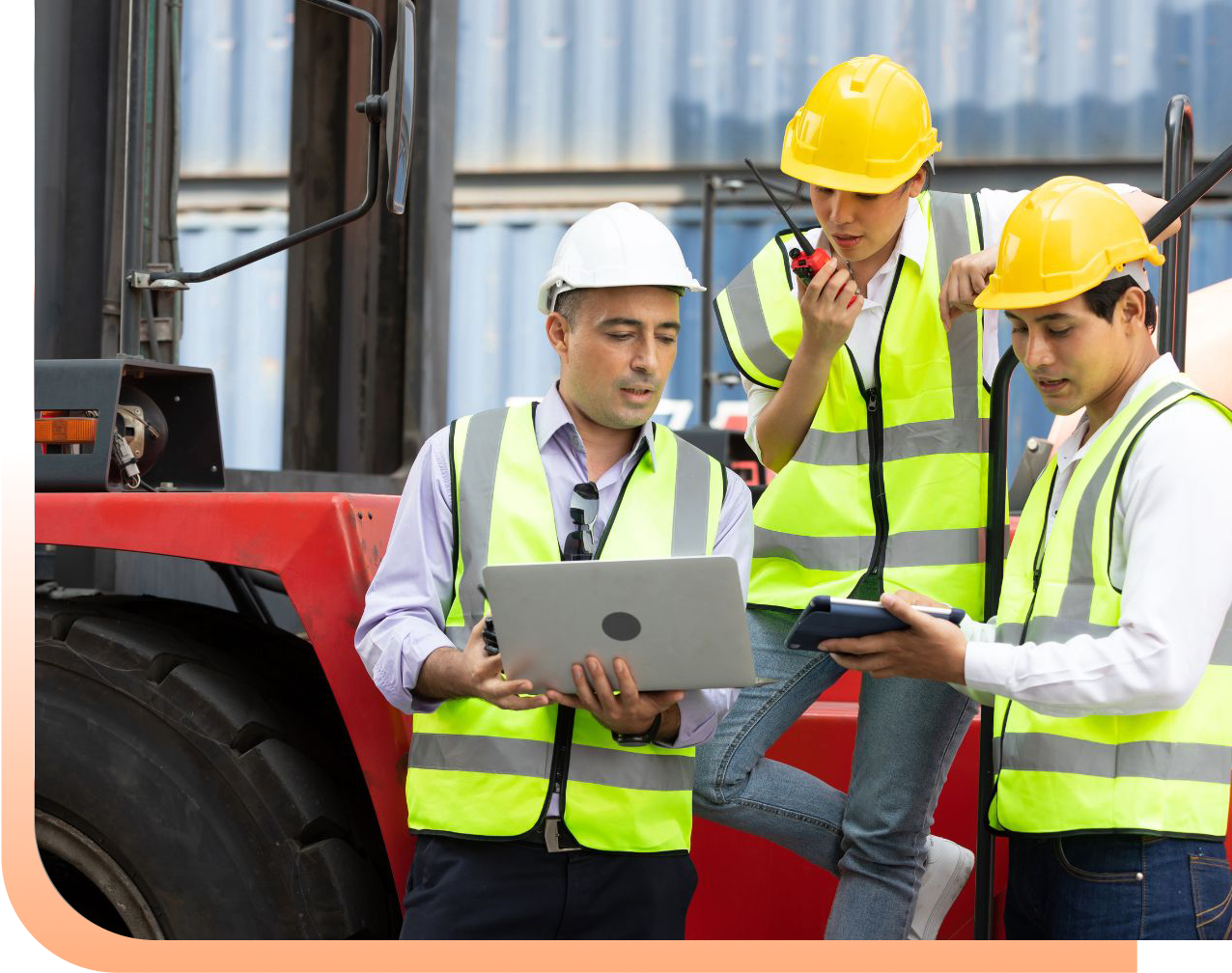 Three construction workers in yellow hard hats and high-visibility vests review plans on a laptop at a site with a red forklift nearby.