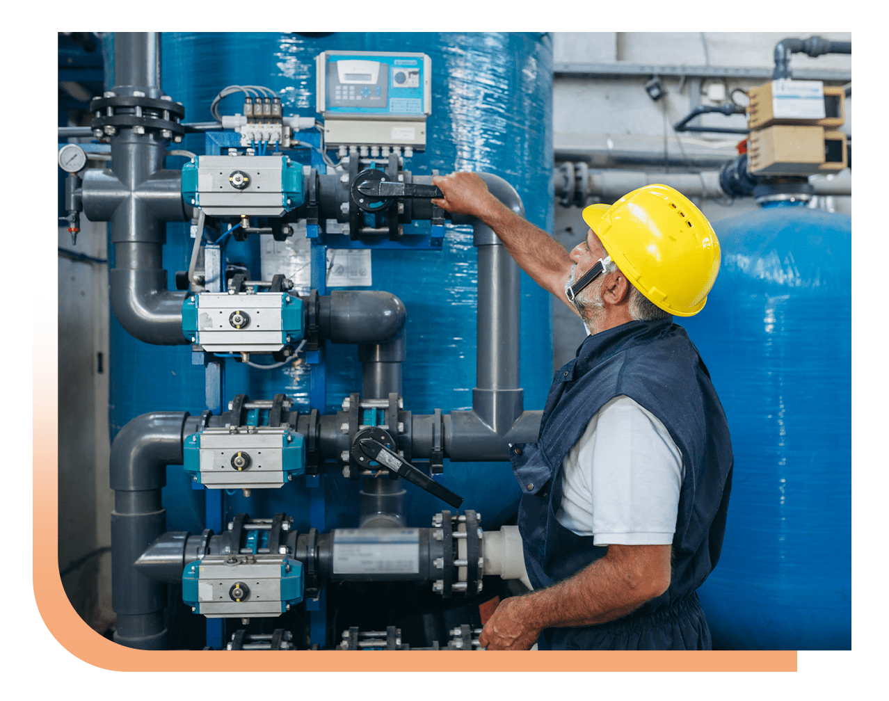 Maintenance worker in a yellow hard hat adjusting blue industrial valves and pipes in a plant setting